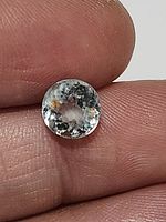 Close-up of the natural unheated blue Aquamarine gemstone held between fingers, showing internal inclusions and round faceted cut.