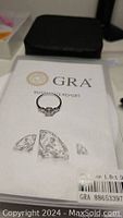 Photo of the moissanite ring on top of GRA certification report, showing the ring and certification for a 1 carat moissanite stone.
