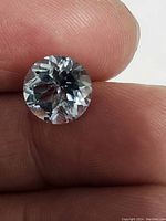 Close-up photo of hand-held round Swiss blue topaz displaying diamond cut facets and light blue color.