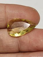 Close-up of the lemon citrine pear cut gemstone held on fingers showing facets and color.