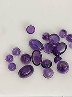 Multiple genuine amethyst cabochon gemstones in oval and round shapes laid out on a white surface.