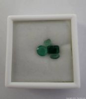 Photo showing five loose emerald gemstones inside a white box with foam padding.