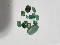 Loose genuine emerald gemstones laid out on white background showing various sizes and cuts.