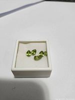 Four pear-shaped peridot gemstones displayed in a small white box on a white background.