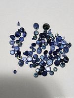 Collection of loose genuine sapphire gemstones in various sizes and blue shades scattered on white background.