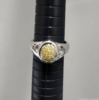 Silver ring on ring sizing stick, showing size 7. Oval cluster of small diamonds as centerpiece with split shank band design.