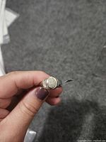 Close-up of silver ring held by fingers showing the oval top with diamond cluster.