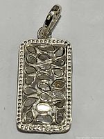 Close-up image of the rectangular silver pendant featuring a beaded border and diamond accents among teardrop shapes.