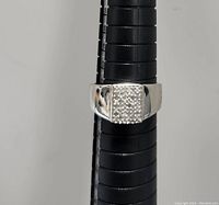 Front-facing photo of silver diamond ring mounted on a black ring sizer showing the square cluster diamond top and polished silver band.