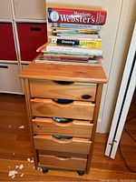 Wooden storage cabinet with six drawers on wheels, topped with stacked art books.