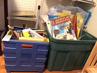 Overview of two plastic bins filled with various art supplies including sketch pads, easels, and books.