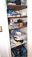 Shelving unit containing folded towels, bedding sheets, and assorted household items packed in bins and baskets.