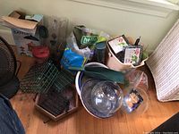 Several bird feeders, suet feeders, bird food bag, fish bowls, scoops, and various containers on a floor near a wall.