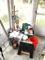 Wide view showing wooden wind chimes on stand, plastic bins containing garden tools and accessories, and a foldable black step stool on floor.