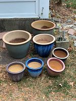 Seven ceramic potting pots of various sizes and colors arranged on the ground outdoors showing their overall appearance and condition.