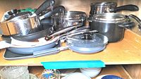 Full view of assorted cookware including pots, pans, and lids stacked and arranged