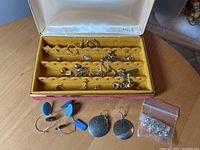 Open red Mele jewelry box showing cream satin lid, gold velvet insert with assorted earrings and items laid out on table