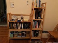 Two wooden folding bookcases with various books and decorative boxes on shelves, viewed frontally in a room with hardwood floor.