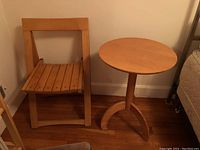 Wooden folding chair next to a round wooden side table, showing side view of chair and table.