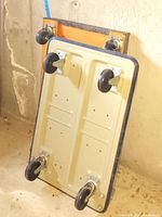 View of the underside of the wooden framed furniture dolly showing four black caster wheels and natural wood frame.