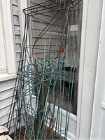Metal garden trellises leaning against wall near door, showing size, design and condition with visible rust and weathering.