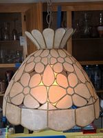 Full front view of dome-shaped capiz shell swag lamp illuminated in indoor setting.