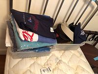 Folded Lands' End shirts, hats on top and in plastic container on mattress