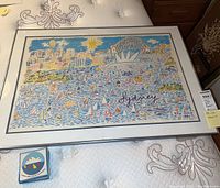 Full view of framed Ken Done artwork depicting Sydney Harbor with Opera House and Harbour Bridge filled with colorful sailboats alongside the set of coasters showing the Sydney Opera House design.