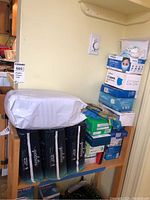 Shelf with multiple boxes of disposable face masks and exam gloves; top shelves show face mask boxes, middle and bottom shelves show boxes of gloves and other medical supplies