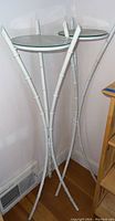 Full view of the two white metal stands with round glass tops showing their height, design and general condition.