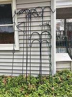 Full view of seven metal plant or birdfeeder hooks against house wall, showing varying heights and decorative styles.