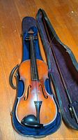 Full view of vintage violin inside open hard case, showing violin and bow compartment.