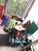 Full overview of garden tools and supplies stacked including hoses, knee cushions, sculptures, watering can, leaf hauler, wooden tools, and cardboard bags in the background.