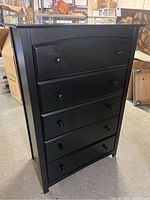 Black tall boy dresser showing front with five drawers and round knobs