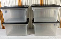 Four clear Sterilite plastic file boxes stacked in two pairs, showing translucent sides and black lids.