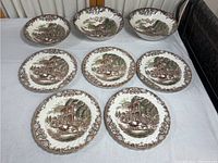 Photo of eight ironstone plates arranged on a flat surface, each with heritage hall scene and decorative floral border.