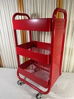 Side angled view showing the three red mesh shelves and pegboard side panel, along with caster wheels.