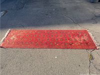 Photo showing the full length of an ornate red runner rug laid out on asphalt, with sun fading and some edge wear visible