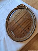 Full view of the oval wall mirror lying flat showing the gilt frame and crest top detail.