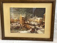 Framed vintage print in wooden frame showing a snowy village landscape scene with people and buildings.
