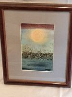 Full view of framed print featuring abstract city skyline with large sun or moon above, wood frame and matting included.