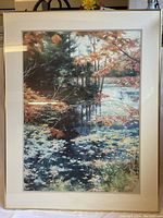 Framed print showing a detailed river scene with trees and water reflections, surrounded by a white mat in a gold-tone frame.