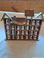 Front view of wooden house-shaped display case labeled 'Thimbleville' holding 23 porcelain thimbles each with different designs.