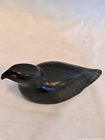 Front-side view of dark soapstone bird sculpture showing overall form and painted eye detail.
