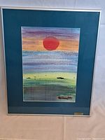 Framed watercolour showing a stylized sunset with a prominent red sun and horizontal bands of color, matted and framed with glass and brass plaque.