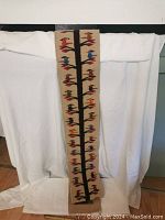Full view of the long narrow tapestry showing the full design with a vertical tree trunk and colorful birds along both sides on a beige woven background.