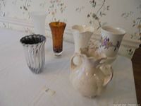 Photo showing all 6 vases arranged on white table with floral wallpaper background, showing variety of shapes, colors, and styles.