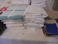 View showing folded assorted towels including white, blue, beige, striped and solid colored towels stacked on a flat surface.