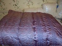 Purple silk-like comforter with stitched floral design spread out on a bed, showing texture and condition