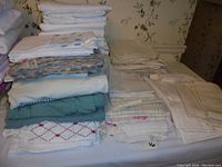 Shows the assortment of folded bed linens stacked on a table including white sheets, patterned sheets, beige and green linens.